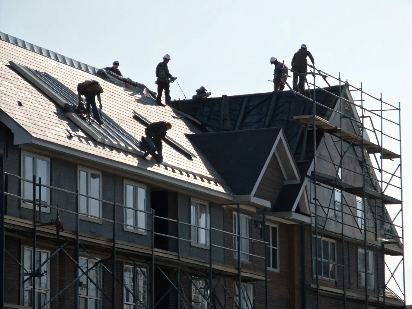 Workers on a large roofing project installing shingles.